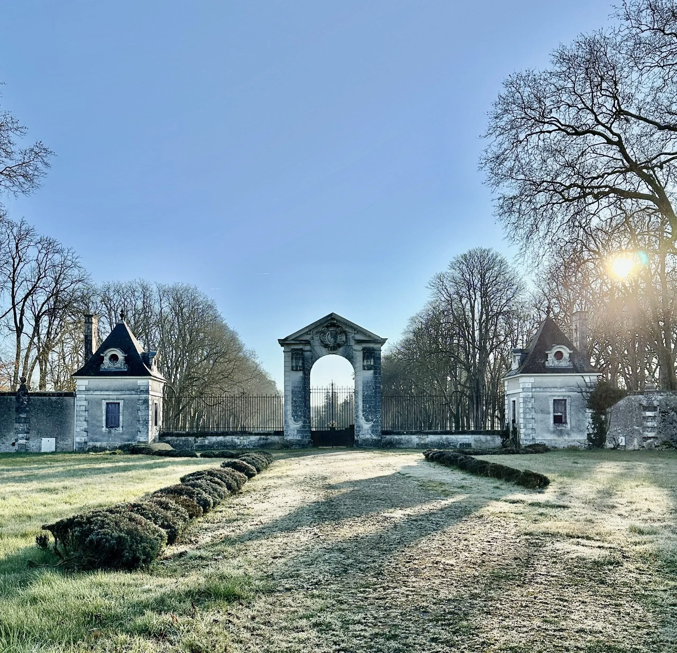 Entrée majestueuse d'un domaine historique avec archère et pavillons en pierre.