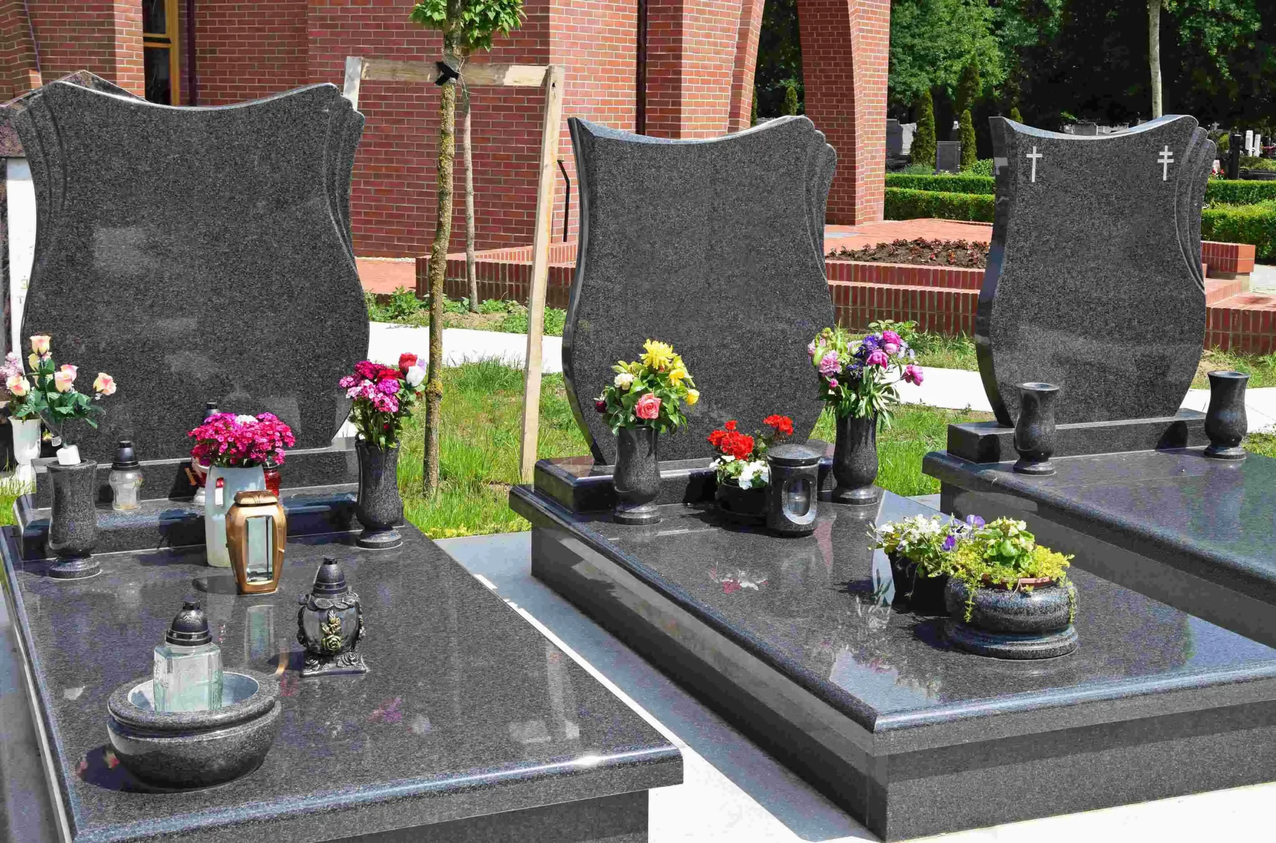 Tombes en granit sombre ornées de fleurs colorées et de lanternes dans un cimetière.