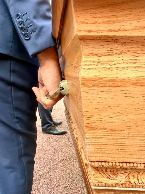 Gros plan sur un porteur funéraire tenant la poignée d'un cercueil en bois.