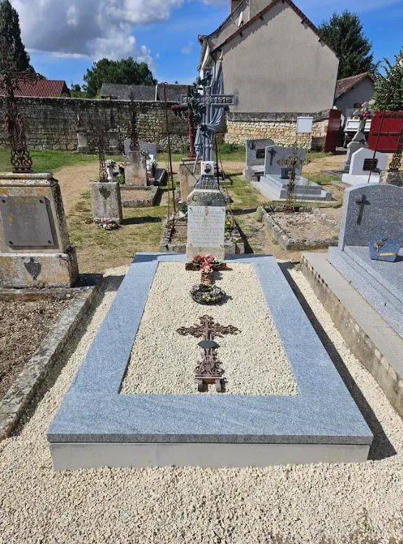 Tombe rénovée avec dalle en granit clair et croix en fer forgé dans un cimetière.
