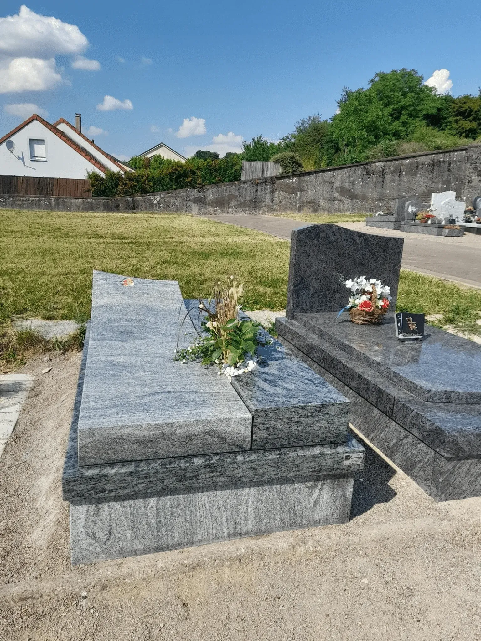 Monument funéraire contemporain en granit gris veiné dans un cimetière ensoleillé.