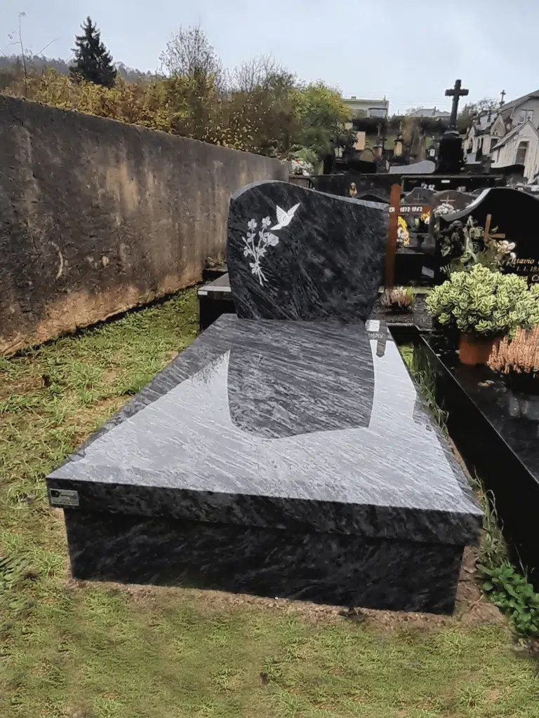 Sépulture en granit gris nuancé gravée d'une colombe et de fleurs blanches.