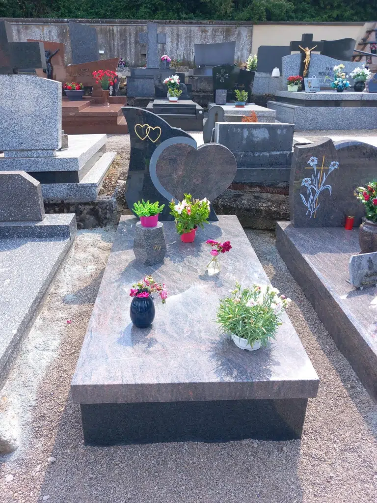 Tombe en granit avec stèle en forme de cœur ornée de deux cœurs dorés et fleurs.