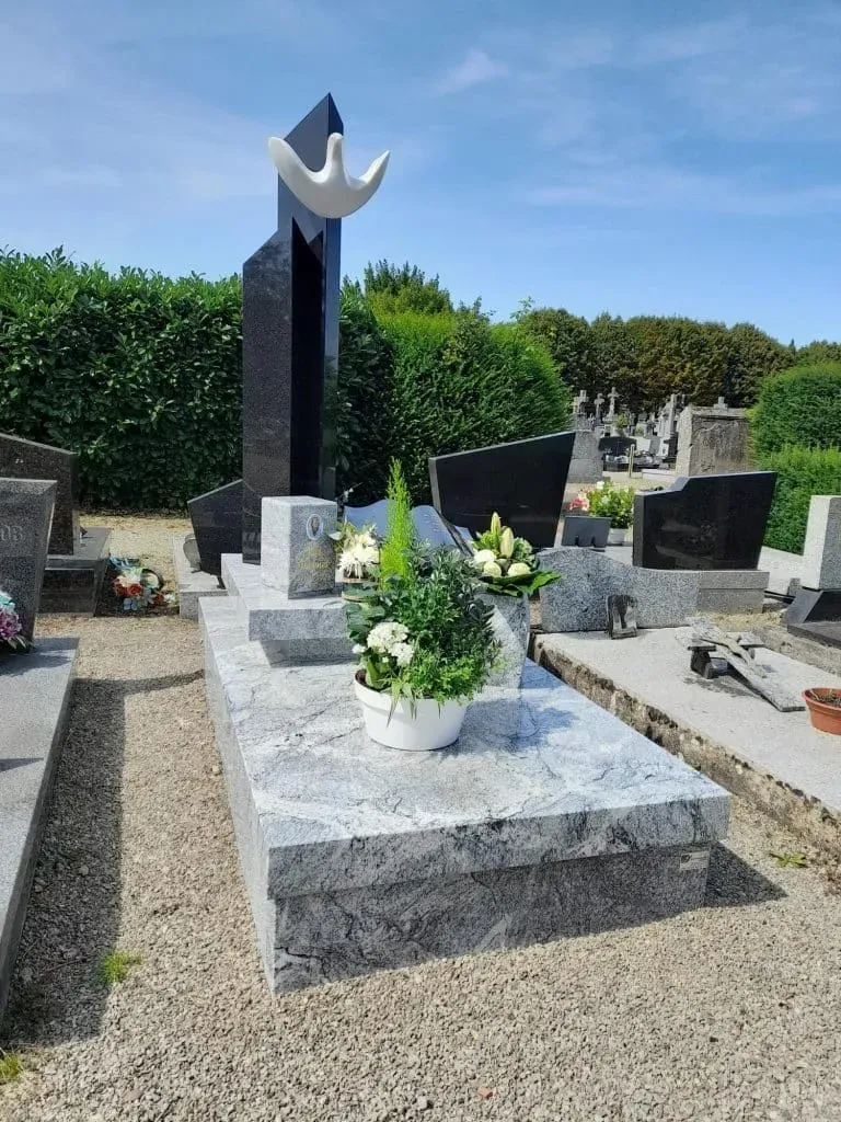 Monument funéraire moderne en granit gris sculpté d'une colombe blanche au cimetière.